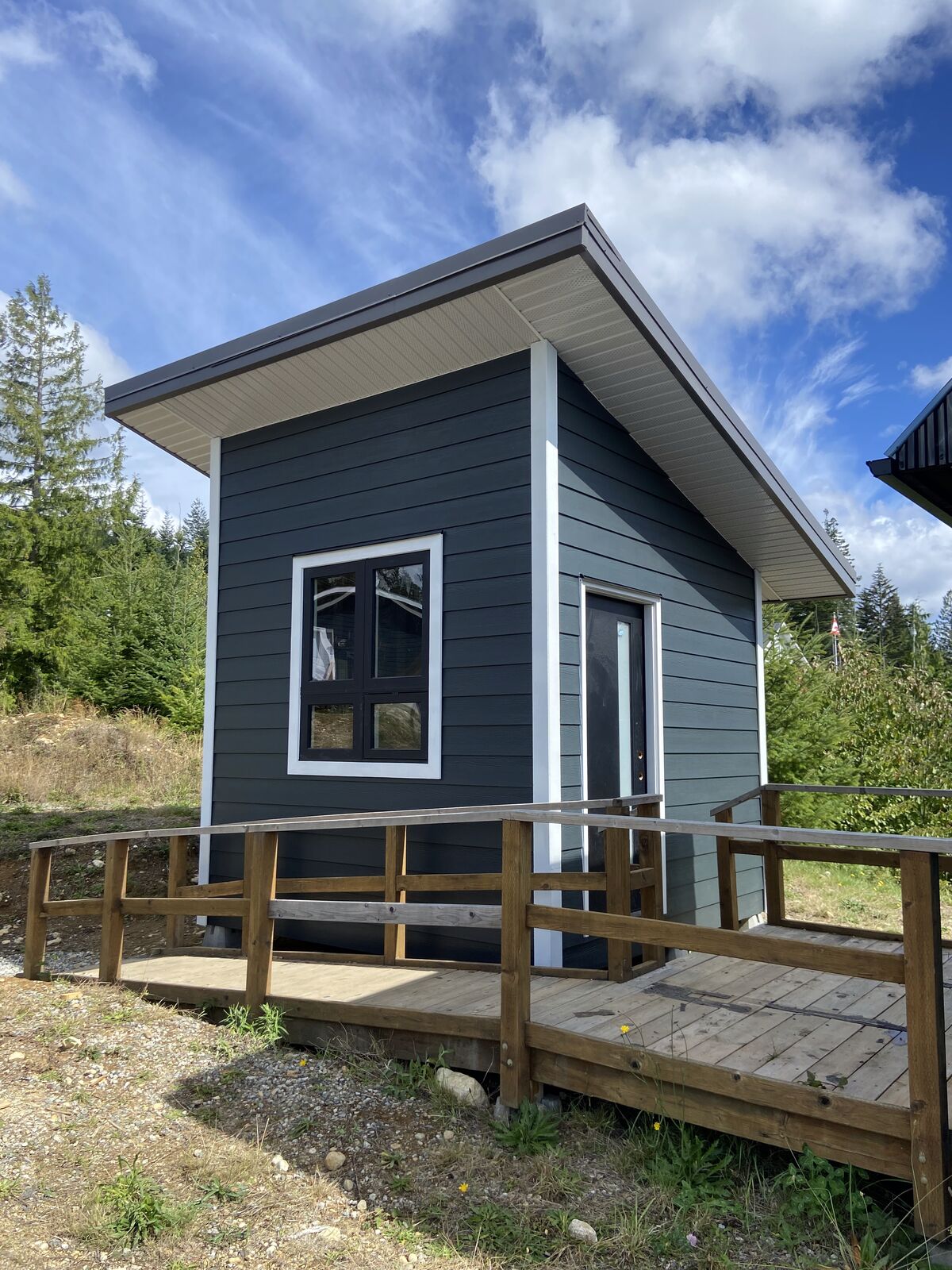 A finished backyard bunkie by Korey Cotnam, with dark siding, white trim and a wooden ramp