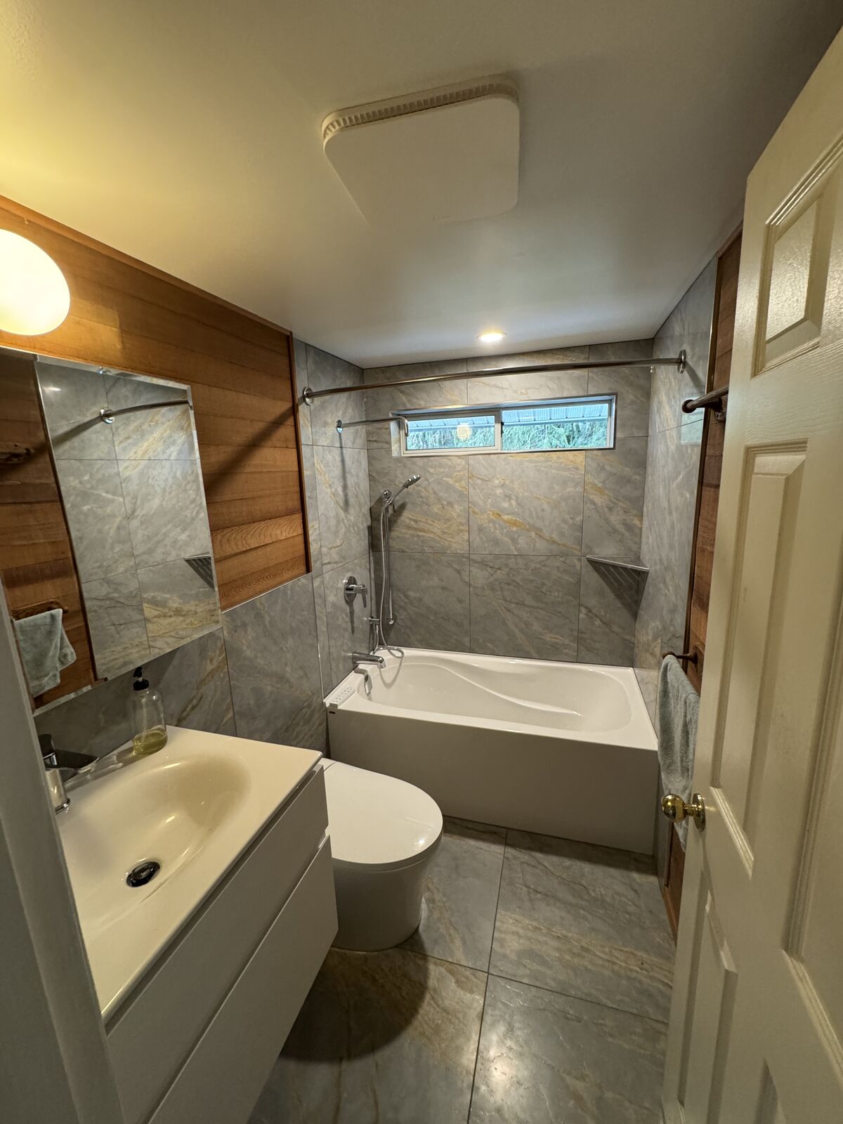 Renovated bathroom with tiled tub surround and wood accent wall